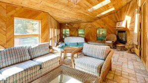 A cozy wooden cabin interior with a sofa, wicker chairs, a hot tub, and a fireplace.