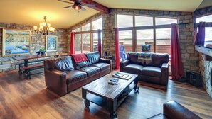 A spacious living room with leather sofas, a wooden coffee table, and a stone wall. - Prairie-style Home on Garden Bay w/ Deck + Hot Tub (Garden)