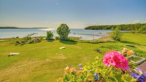 A grassy area with a dock extending into a lake, surrounded by trees and flowers. - Prairie-style Home on Garden Bay w/ Deck + Hot Tub (Garden)
