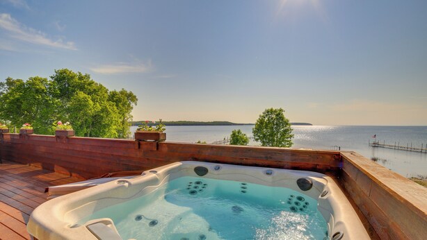 A hot tub with a wooden deck, overlooking a lake with a pier and trees. - Prairie-style Home on Garden Bay w/ Deck + Hot Tub (Garden)