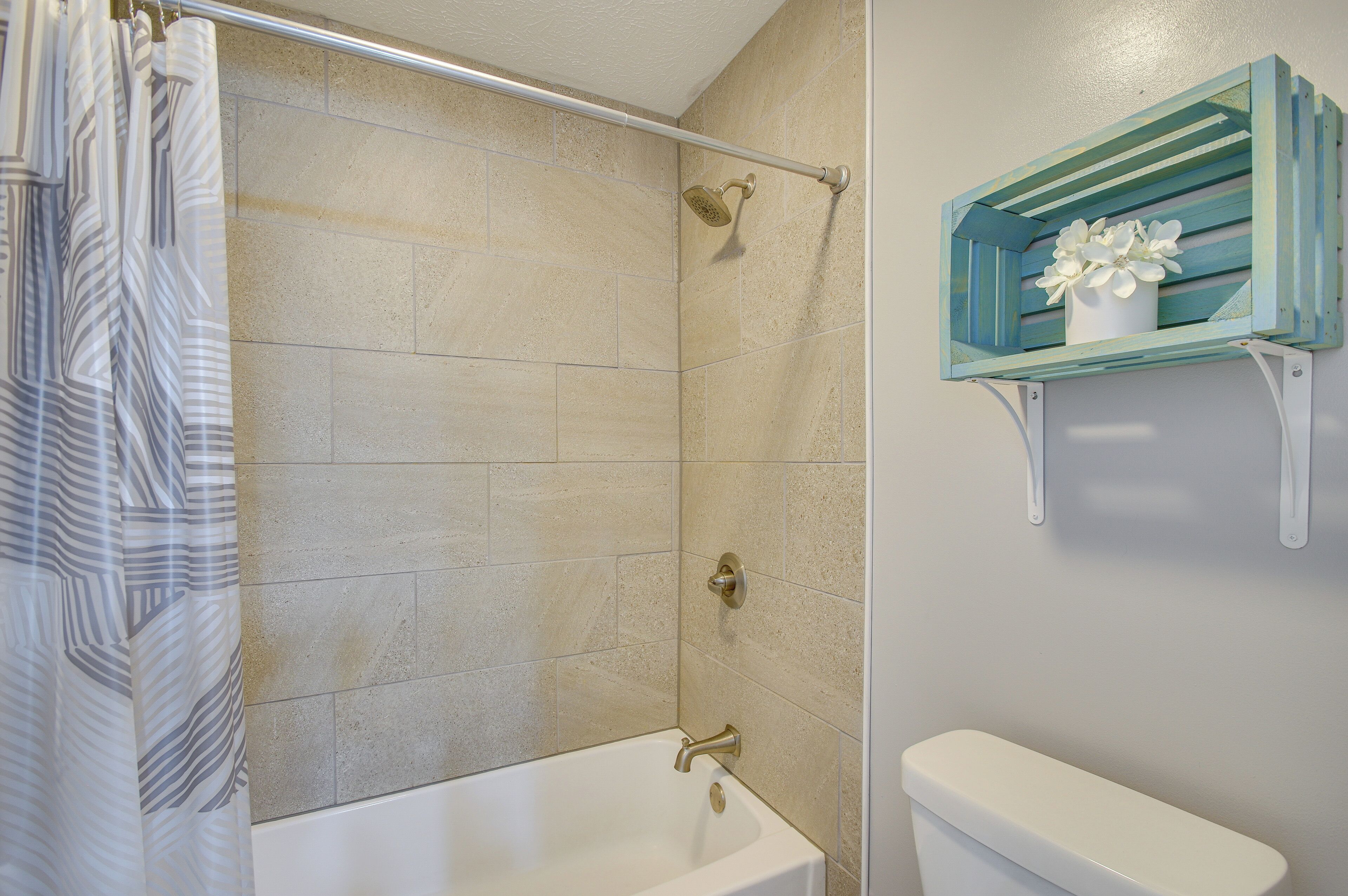 Un baño con ducha, bañera, inodoro y una repisa con un florero.