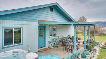 A light blue house with a covered patio area featuring outdoor furniture and a hot tub.