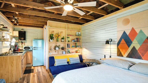 Een gezellige kamer met een bed, een blauwe bank, een keukenhoek en een houten plafond.