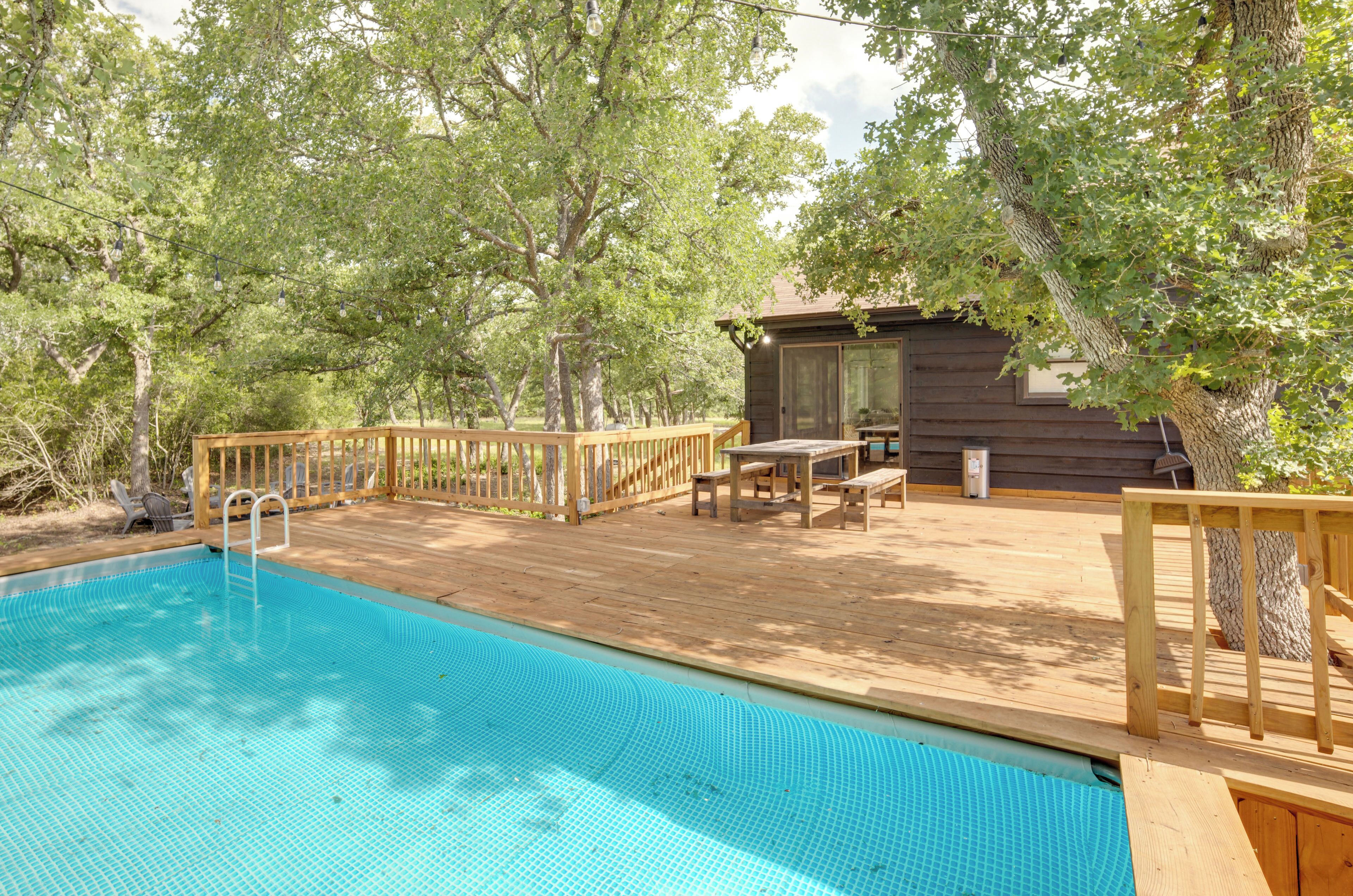 Une terrasse en bois avec une piscine, entourée d’arbres.