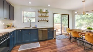 A modern kitchen with dark blue cabinets, a stainless steel dishwasher, and a wooden dining table with yellow chairs. - Somerville Cabin w/ Private Pool! (Somerville)
