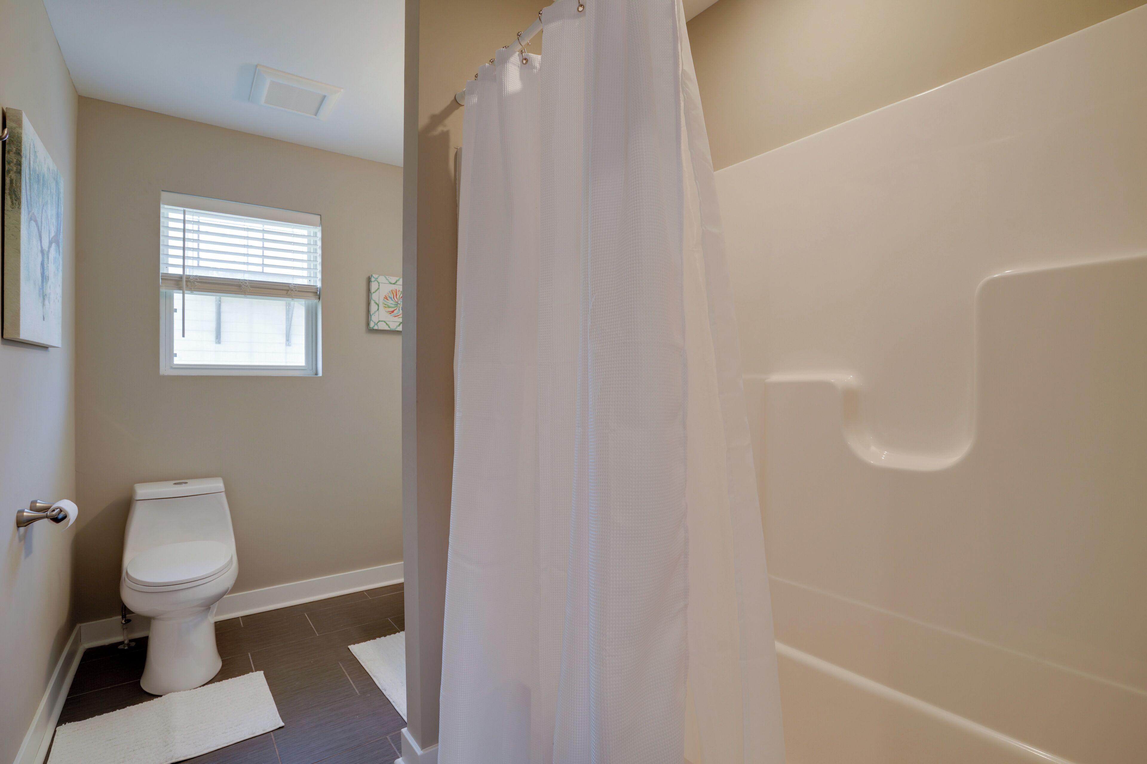 A bathroom with a toilet, a shower curtain, and a window with blinds.
