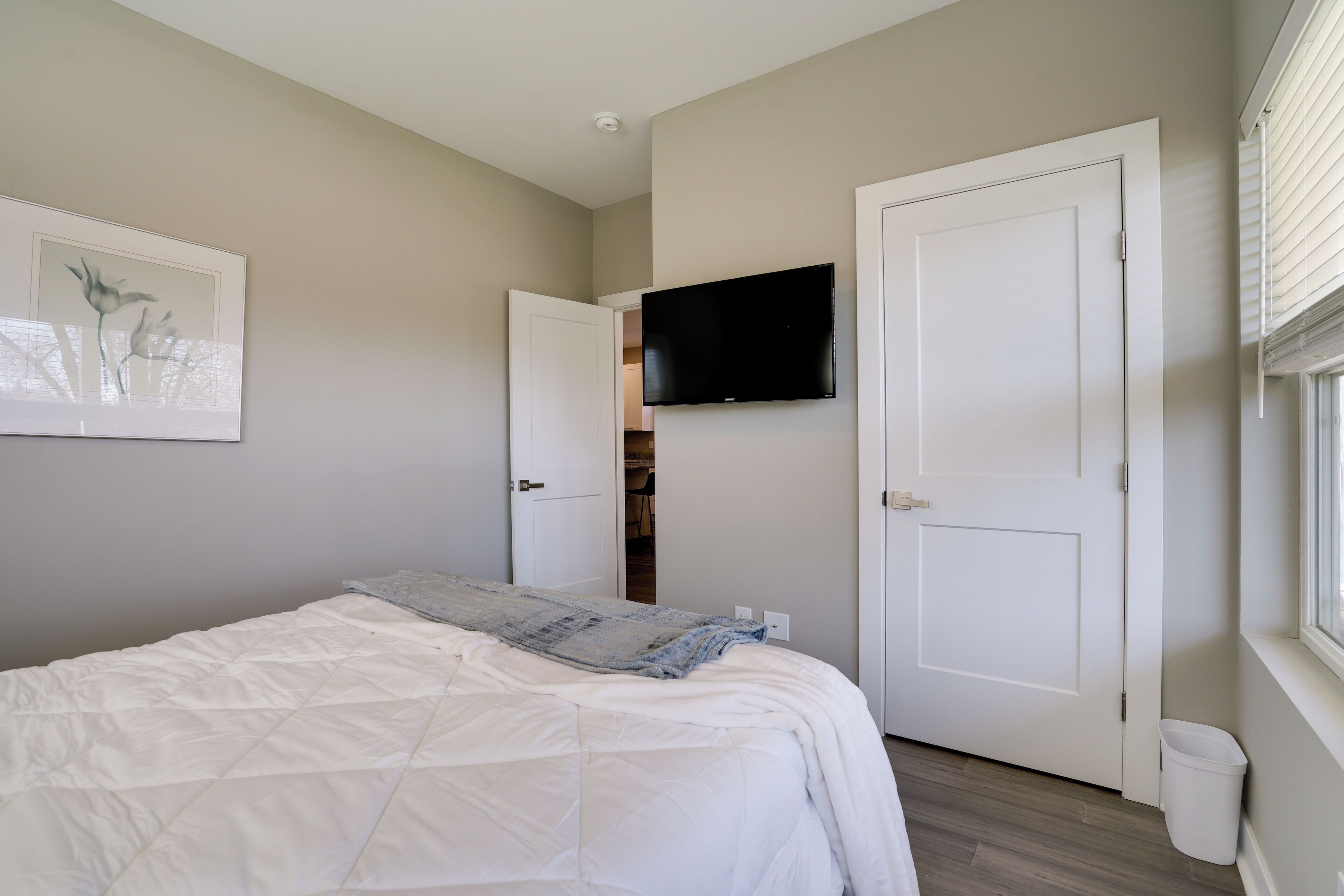A bedroom with a bed, a television mounted on the wall, and a door leading to a closet.