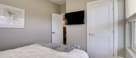 A bedroom with a bed, a television mounted on the wall, and a door leading to a closet.