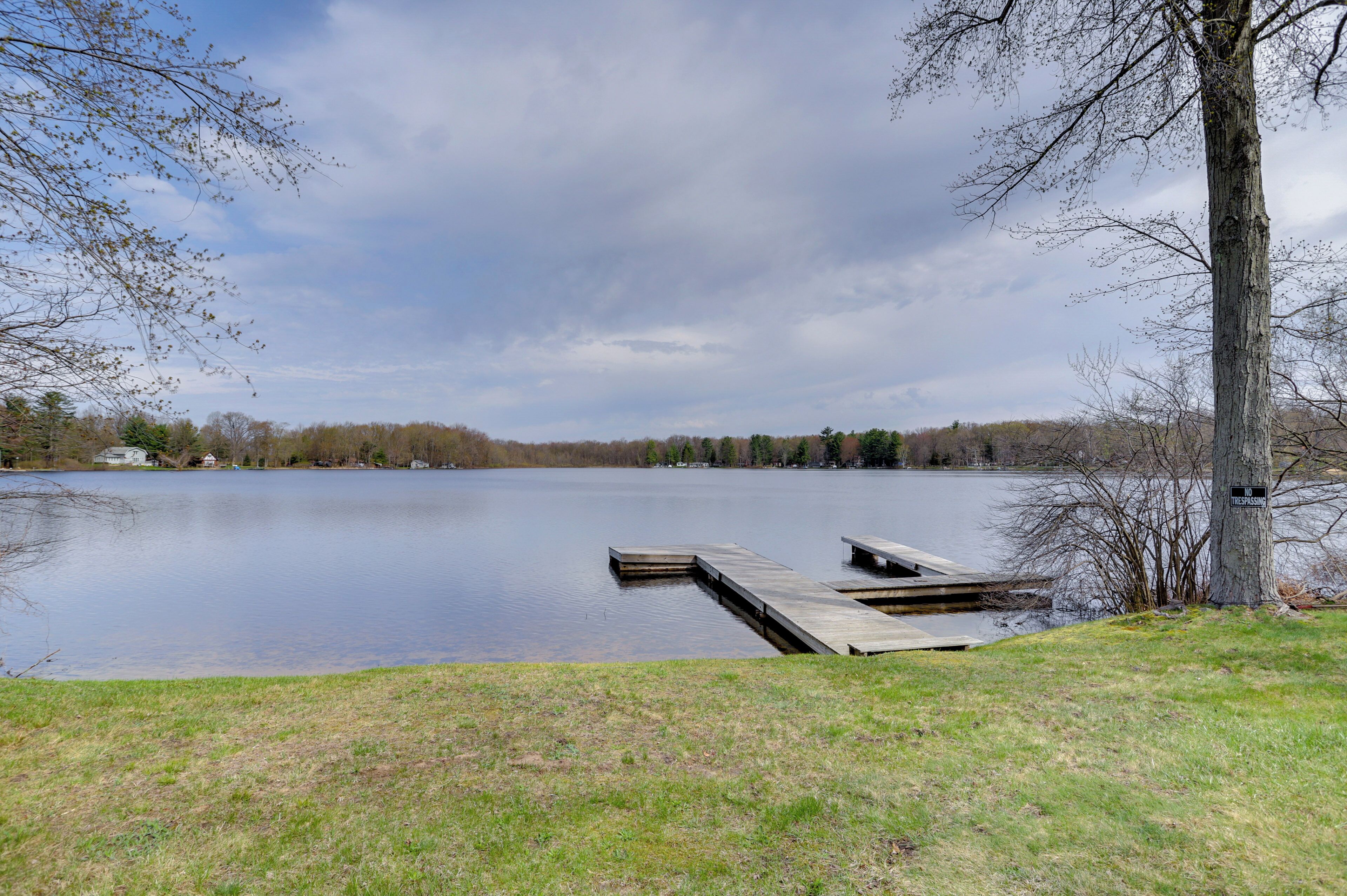 A calm lake with a wooden dock extending into the water, surrounded by grassy banks and trees.