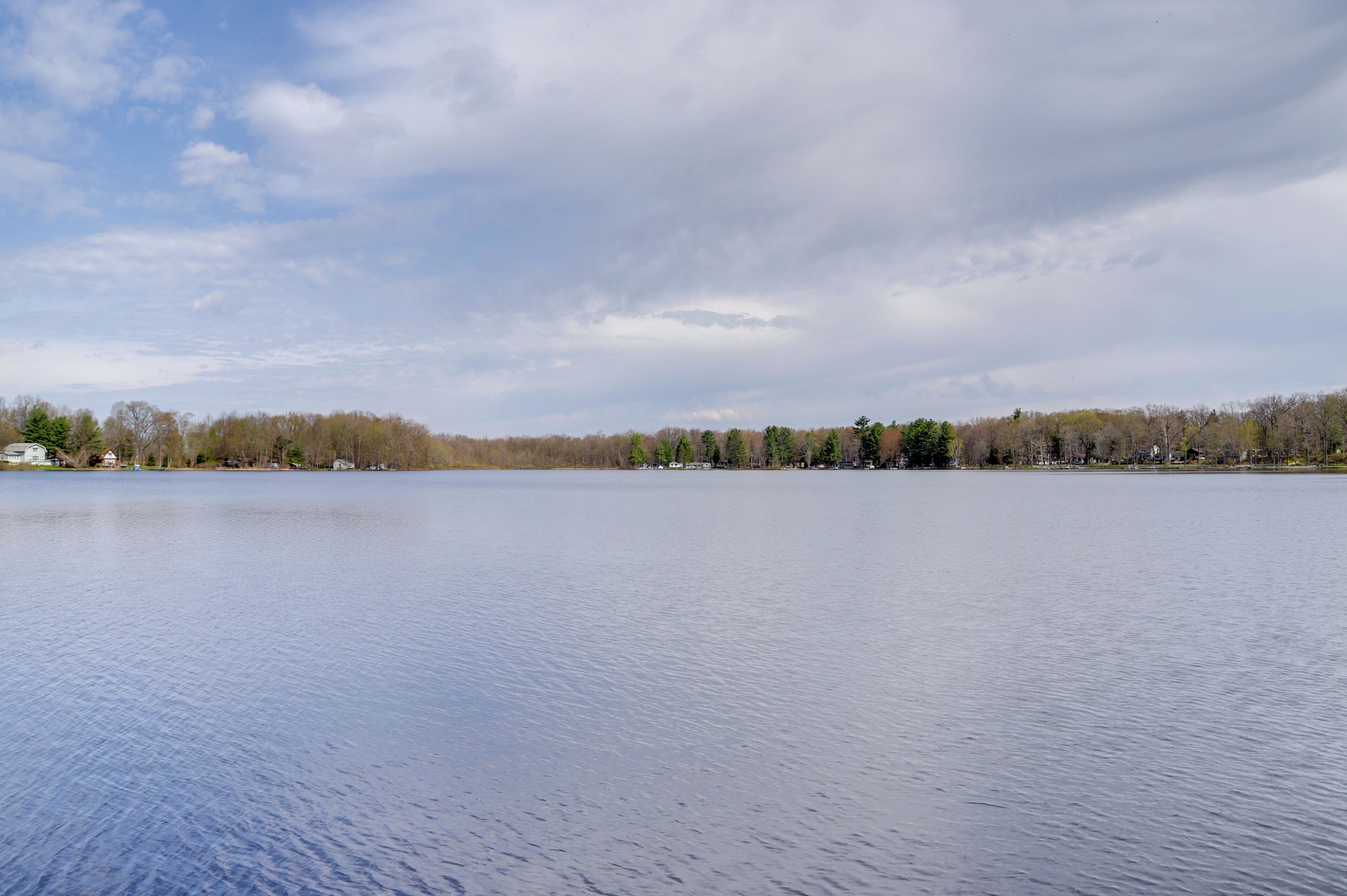 A calm lake with a forested shoreline and a partly cloudy sky.