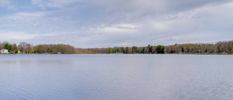 A calm lake with a forested shoreline and a partly cloudy sky.