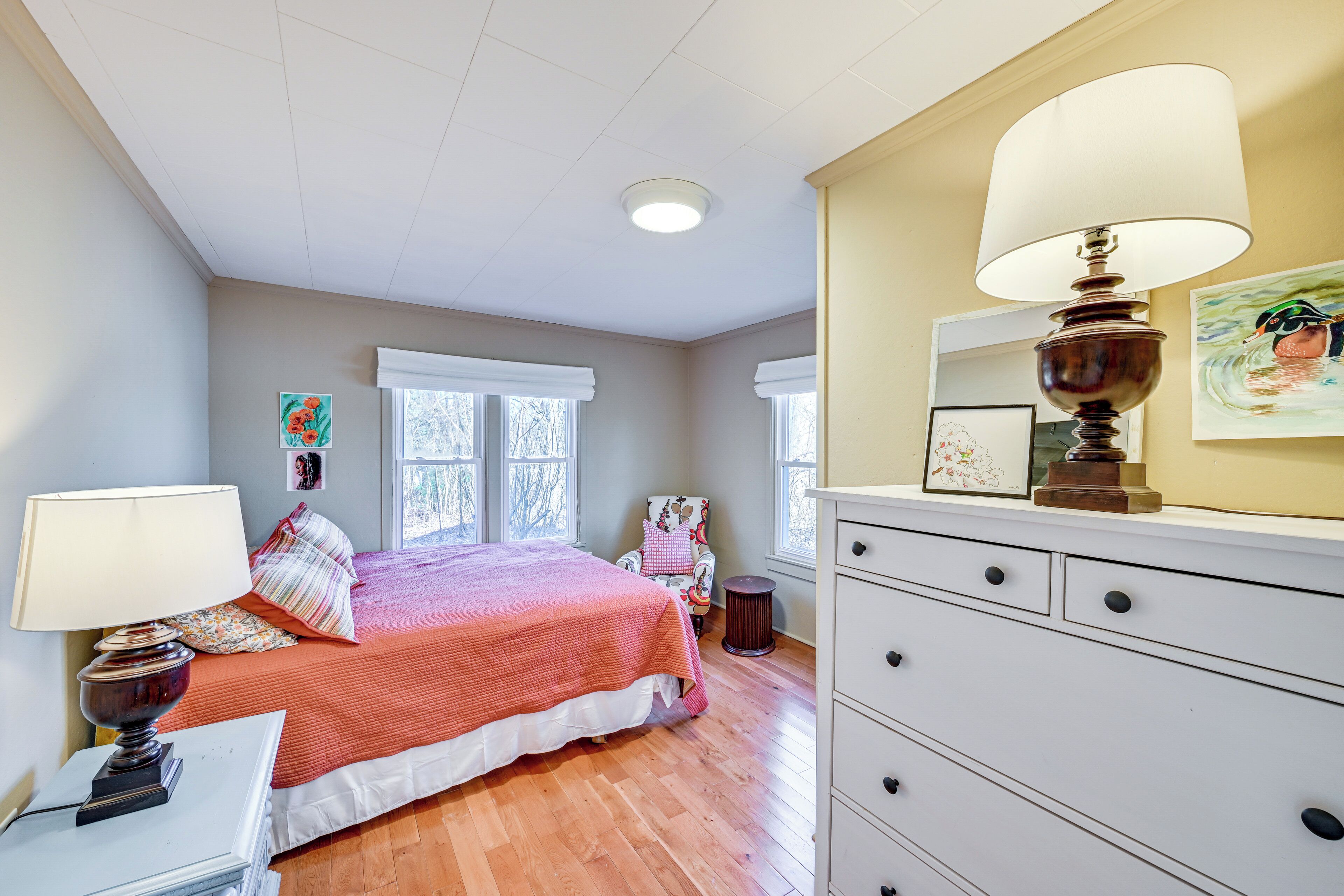 A bedroom with a bed, dresser, lamp, and artwork on the wall.