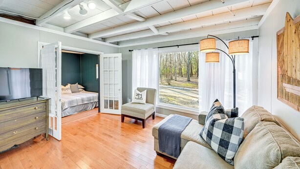 A spacious room with a wooden floor, a bed, a sofa, a chair, and a television. - Grand Junction Lake Home: 13 Mi to South Haven! (Grand Junction)