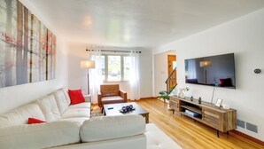 Una sala de estar moderna con un sofá blanco, una mesa de centro de madera y un televisor montado en la pared.
