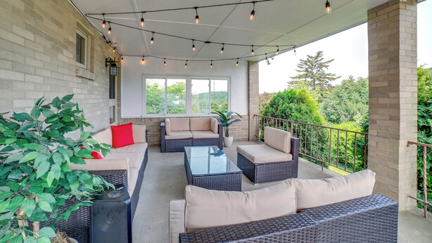 Un patio al aire libre con mobiliario de mimbre, una mesa de centro de vidrio y luces colgantes.