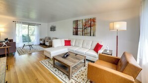 Una sala de estar moderna con un sofá seccional blanco, una mesa de centro de madera y un sillón de cuero marrón.