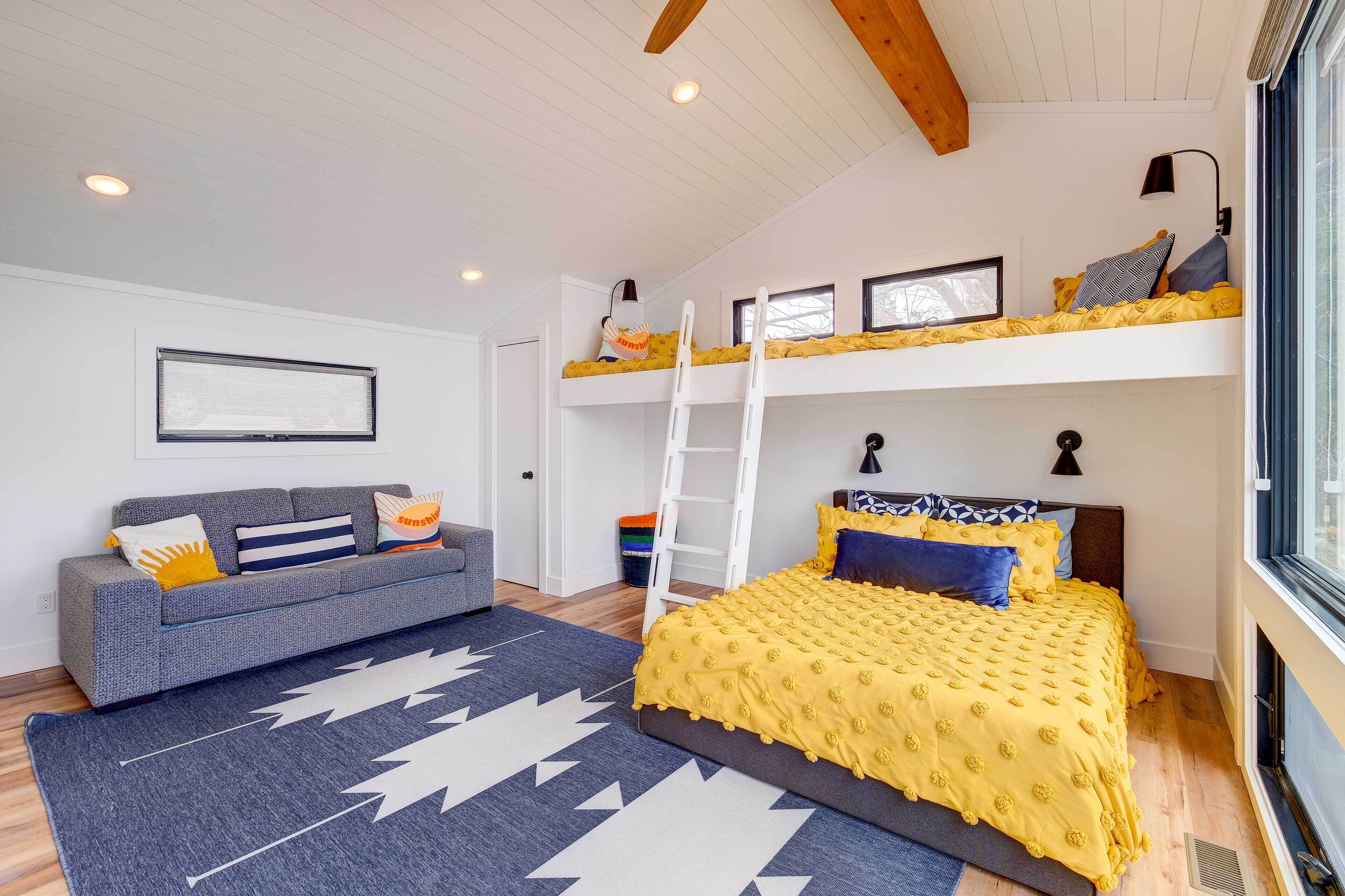 A bedroom with a bunk bed, a sofa, a ladder, and a window.