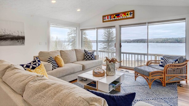 A spacious living room with a large window overlooking a lake, a ceiling fan, and a view of the Charlevoix region. - East Jordan Vacation Rental on Lake Charlevoix! (East Jordan)