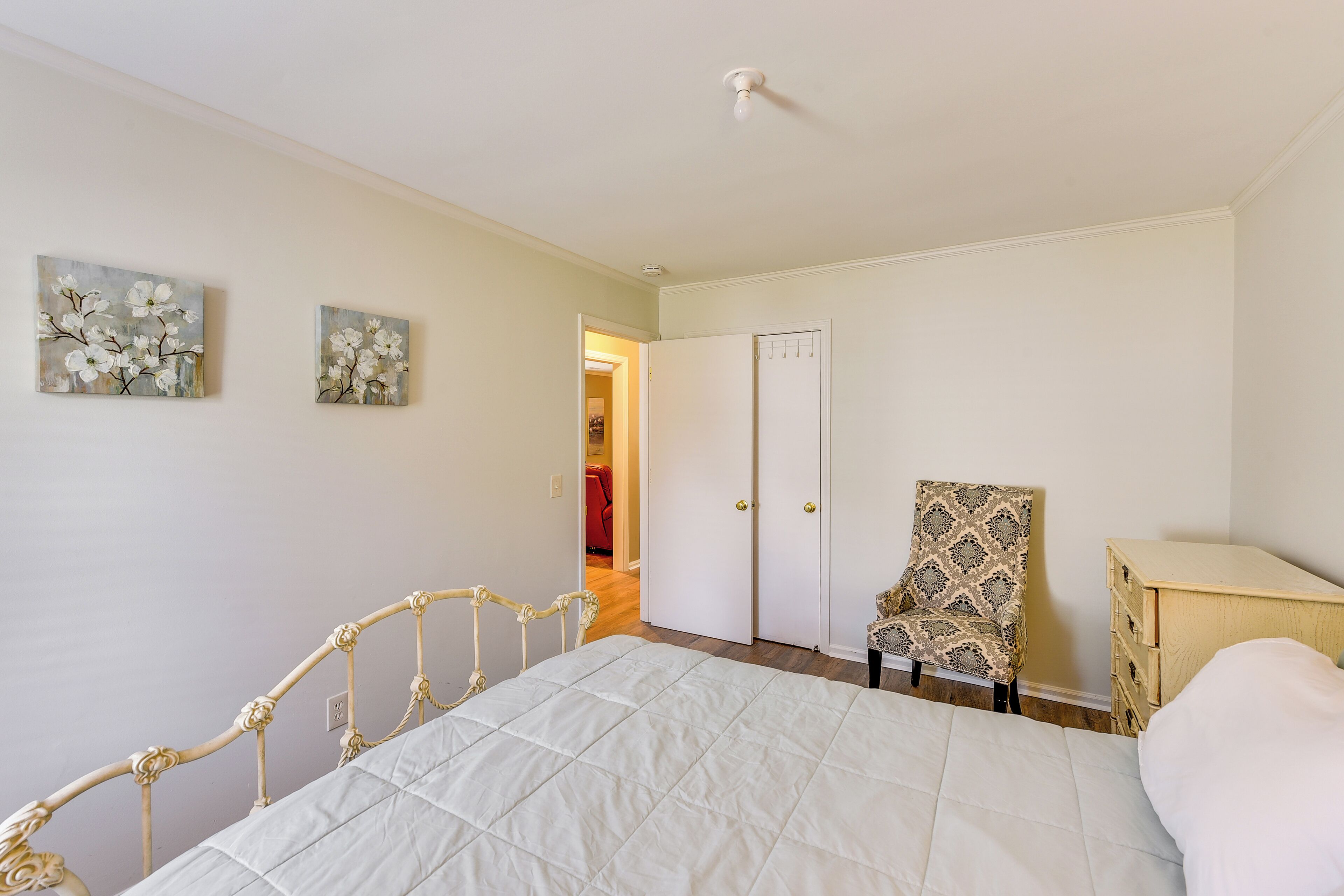 Een slaapkamer met een bed, een kledingkast, een stoel en twee schilderijen aan de muur.