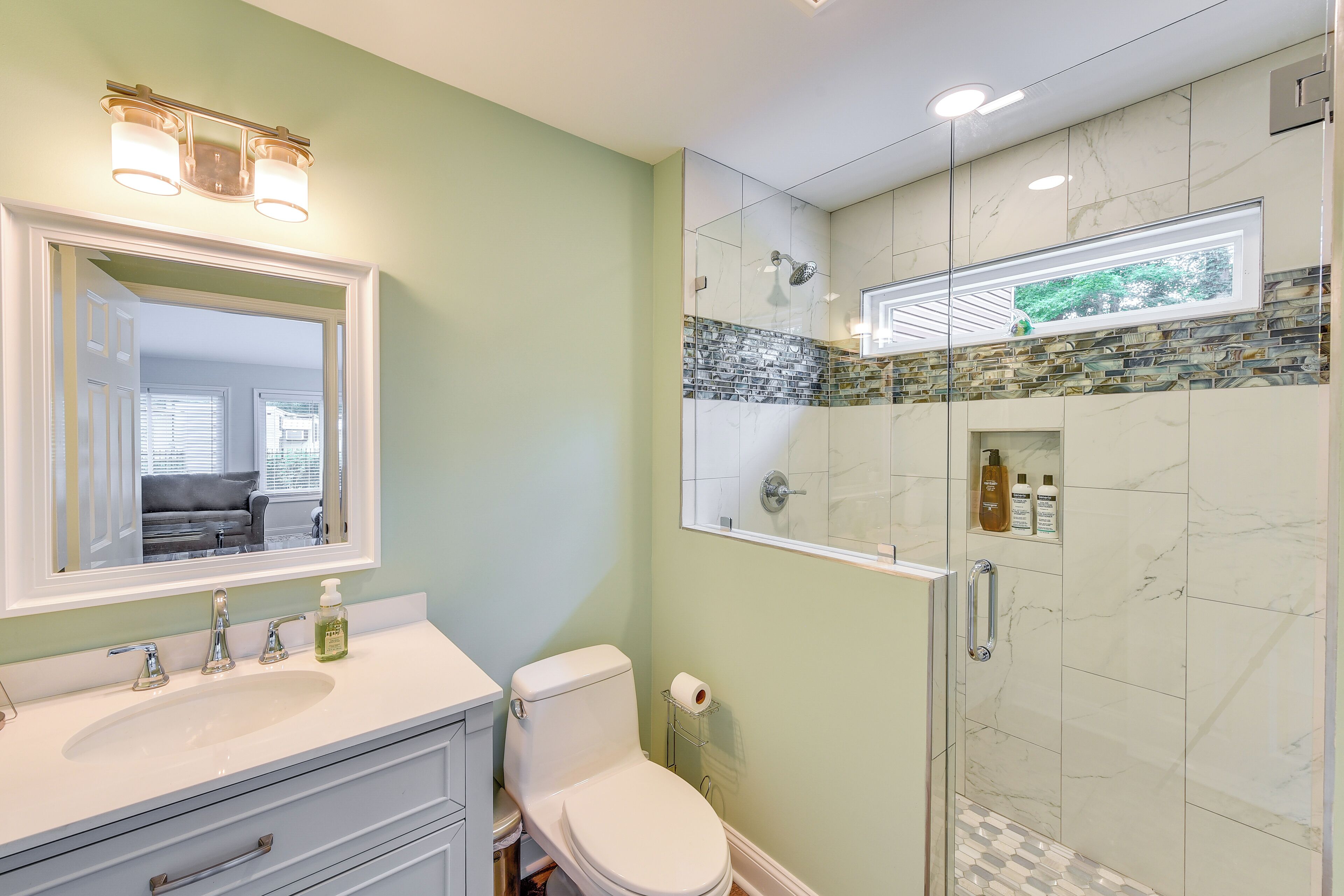 Une salle de bain avec un lavabo blanc, des toilettes et une douche en verre, le mur derrière le lavabo étant recouvert de marbre.