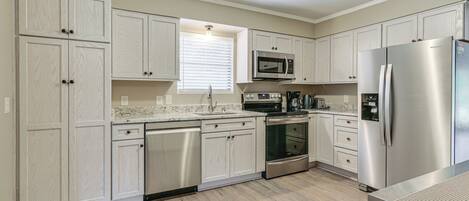 A modern kitchen with light wood cabinets, stainless steel appliances, and a marble countertop.