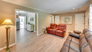 A living room with a brown leather sofa, a floor lamp, and a kitchen visible in the background. - Charming Bluffton Vacation Home w/ Yard! (Bluffton)