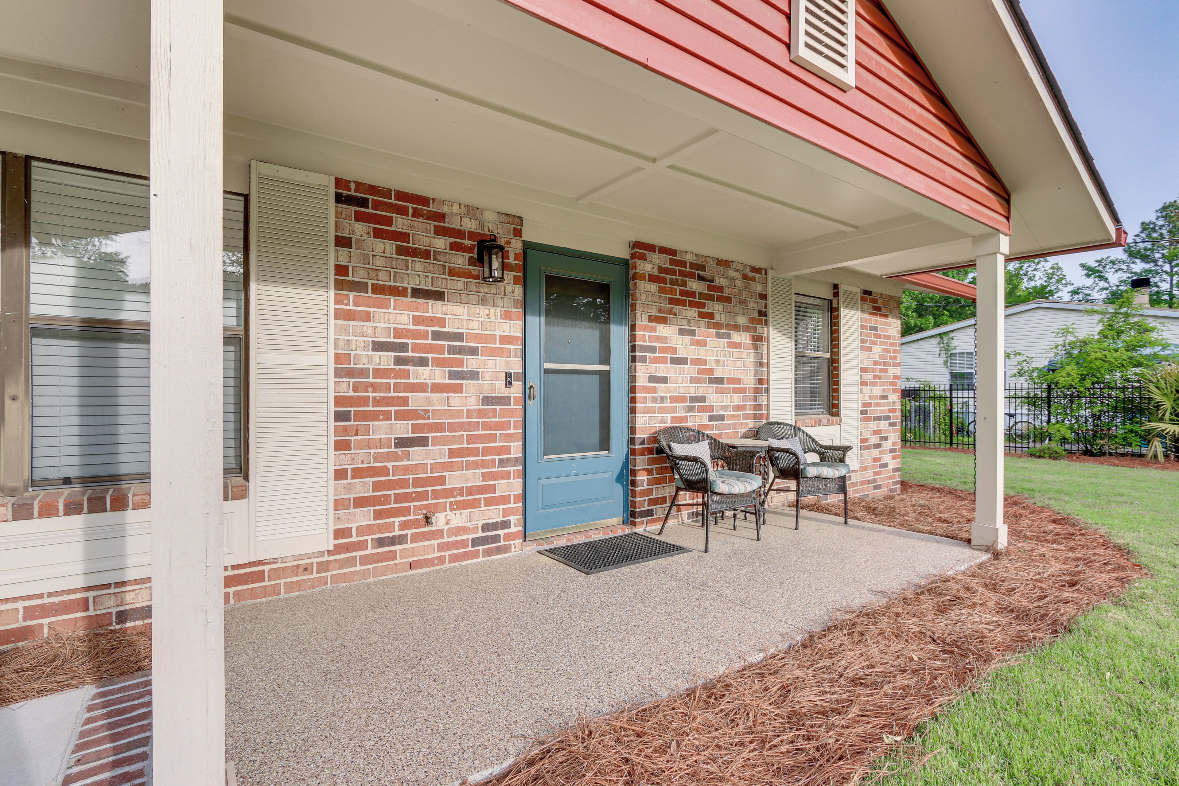 A covered porch with a brick exterior, a blue door, and a small patio area with a table and chairs.