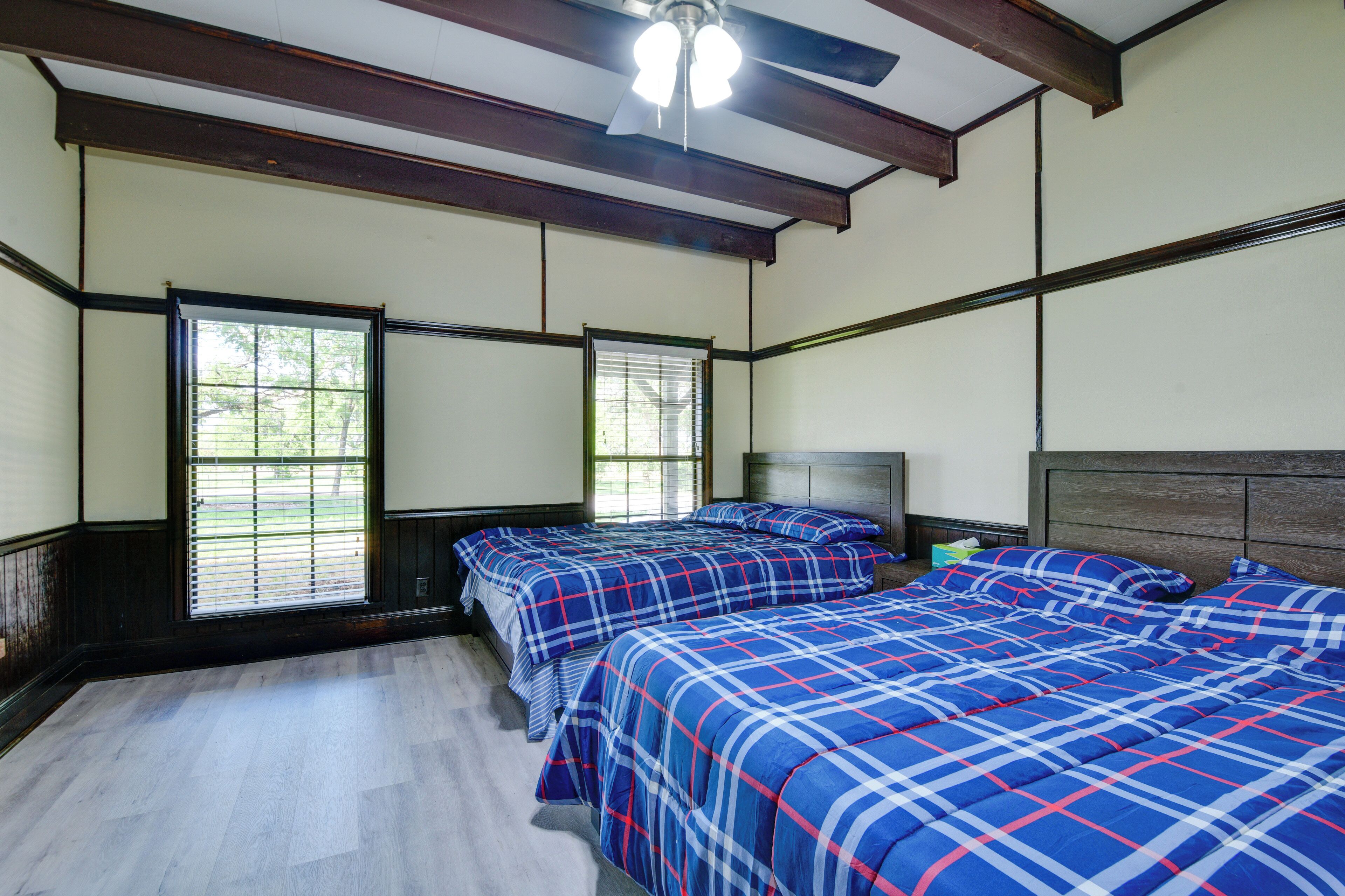 A room with two beds, wooden beams, a ceiling fan, and large windows.