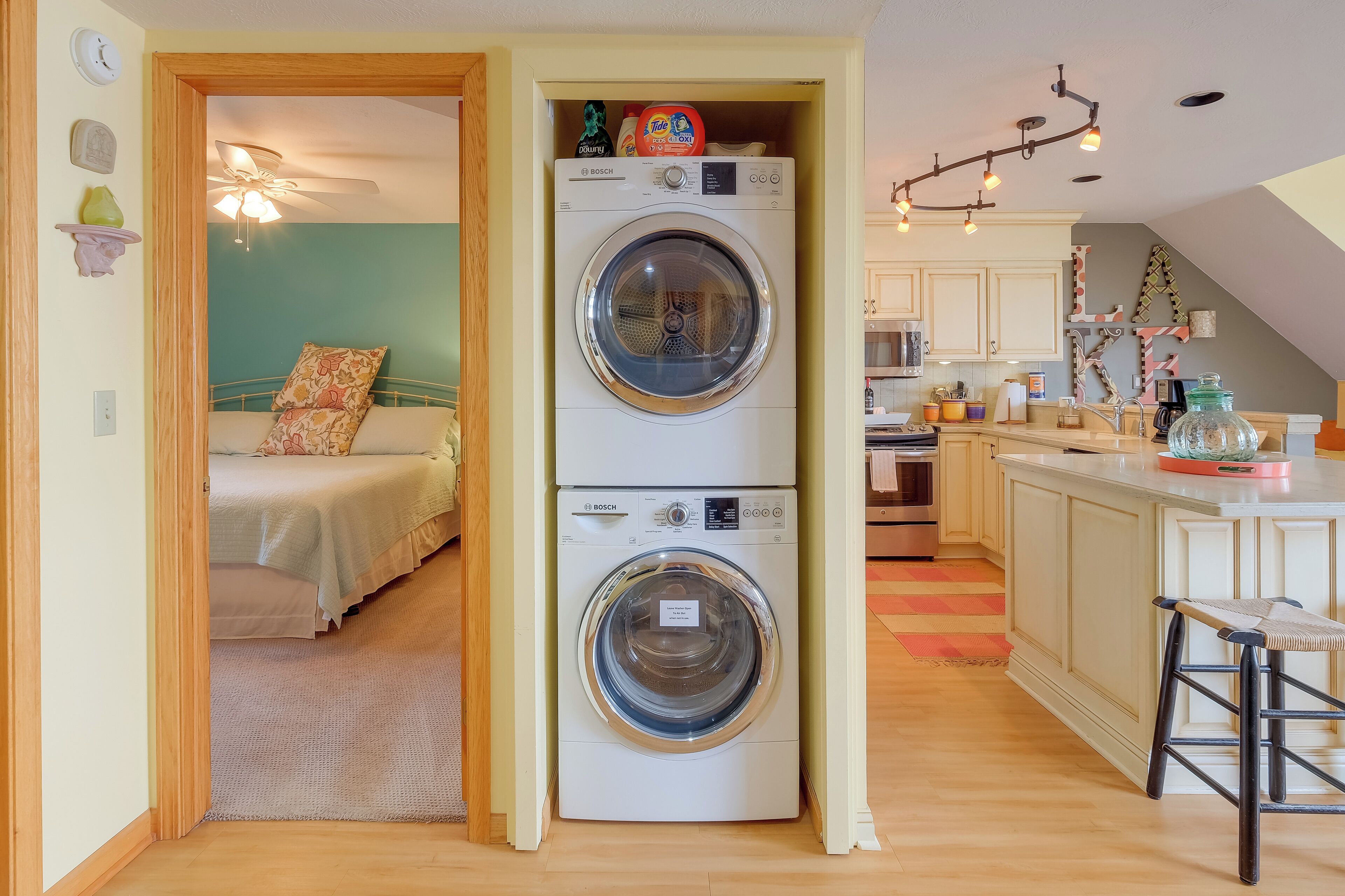 Un appartement compact équipé d’un lave-linge, d’un lit avec une literie à motifs floraux, d’une kitchenette et d’un petit coin repas.