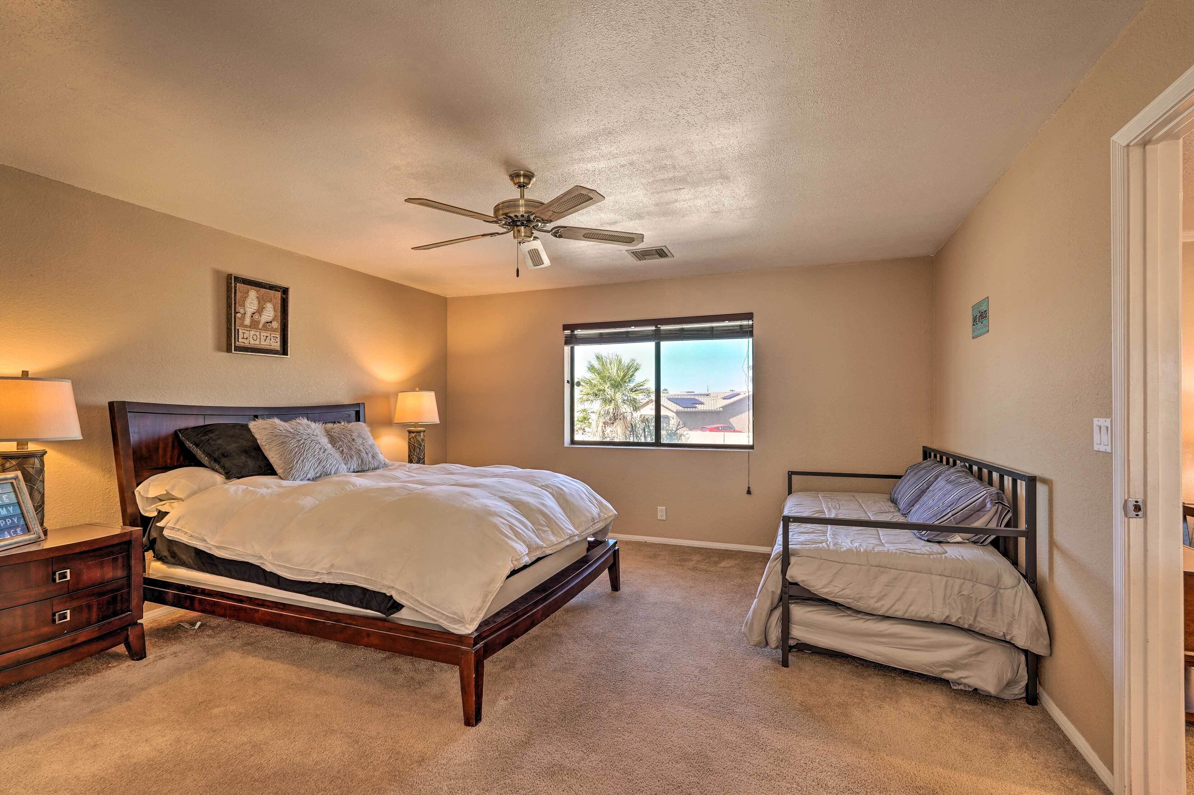 A bedroom with a large bed, a smaller bed, a ceiling fan, a window, and a nightstand with a lamp.