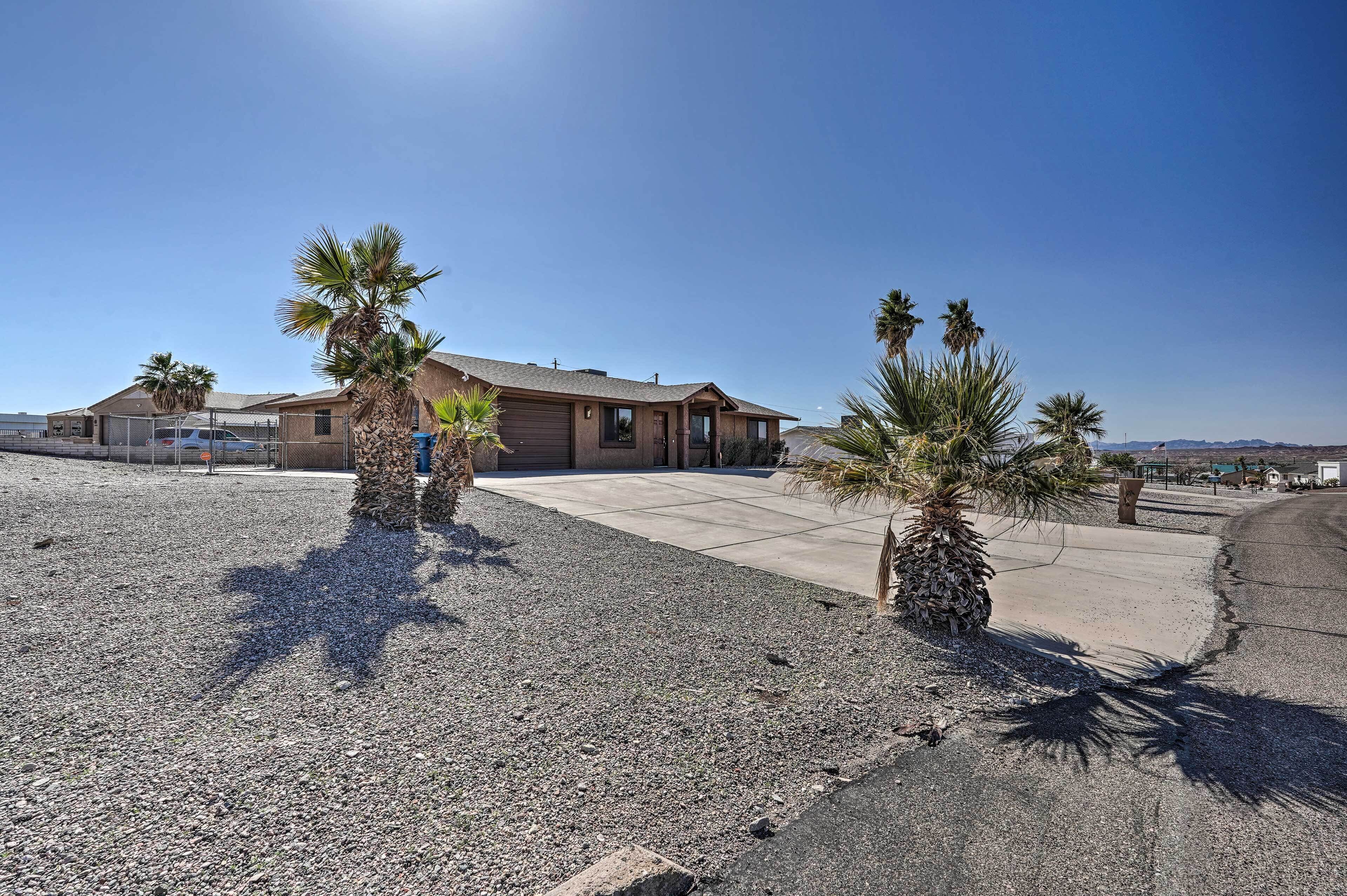 A residential property with a single-story house, a driveway, and a gravel area with palm trees.