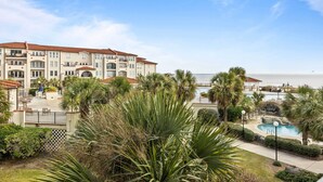 Ein mehrstöckiges Hotel mit Poolbereich, Palmen und Blick aufs Meer.