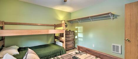 A bunk bed room with a ceiling fan, a dresser, and a wall-mounted shelf.