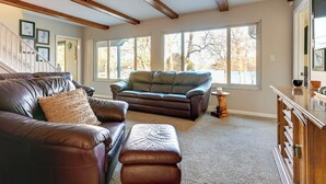 Ein Wohnzimmer mit zwei Ledersofas, einem Holzschrank und großen Fenstern mit Blick auf Bäume.