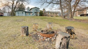 Ein Garten mit einem Feuerkorb, umgeben von Baumstümpfen, ein Haus im Hintergrund und ein klarer Himmel.