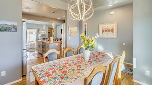 A dining area with a floral tablecloth, wooden chairs, a vase with flowers, and a modern chandelier.