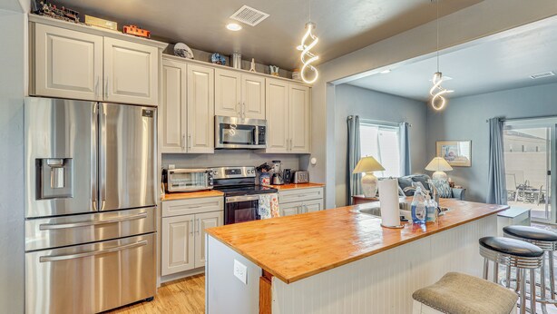 A modern kitchen with stainless steel appliances, a wooden island, and a bar area with stools.