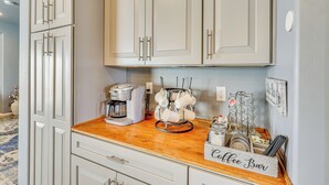 A kitchen with white cabinets, a coffee maker, a mug rack, and a coffee bar sign.