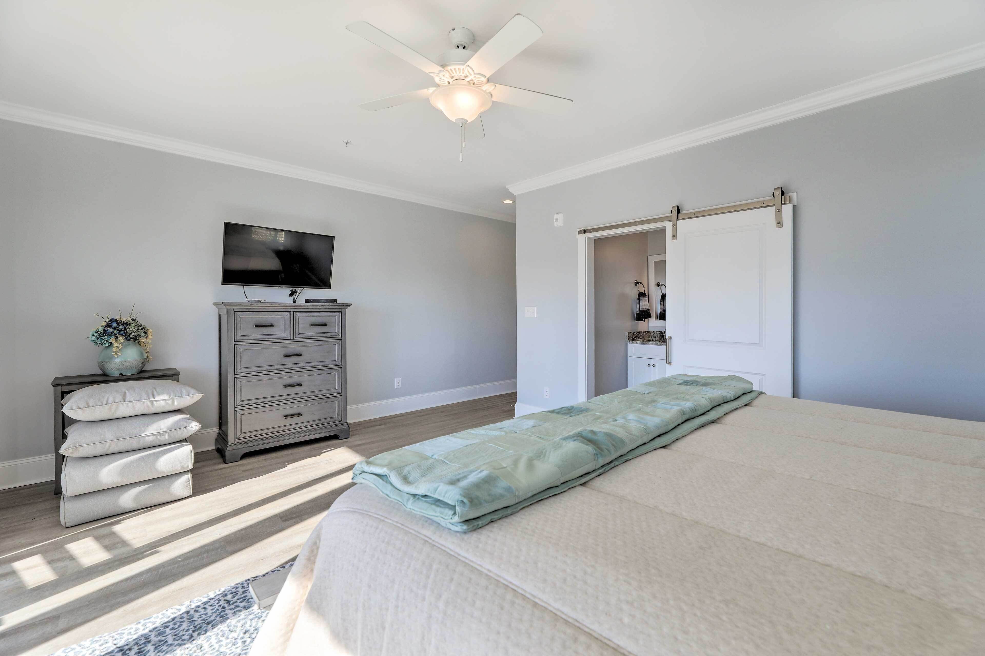 A bedroom with a bed, a dresser, a television, a ceiling fan, and a sliding door.
