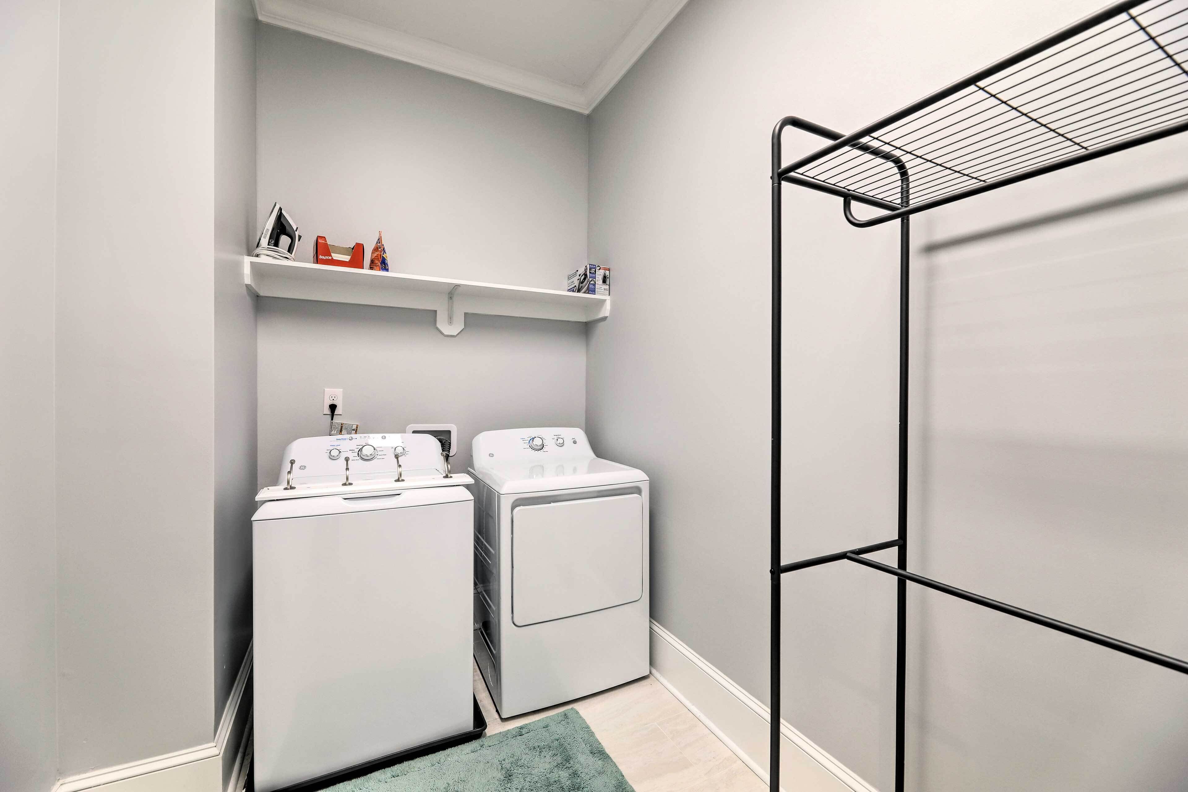 A laundry room with two white washing machines, a shelf with small items, and a black drying rack.