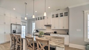 Une cuisine moderne avec des meubles blancs, un îlot en marbre et des luminaires suspendus.