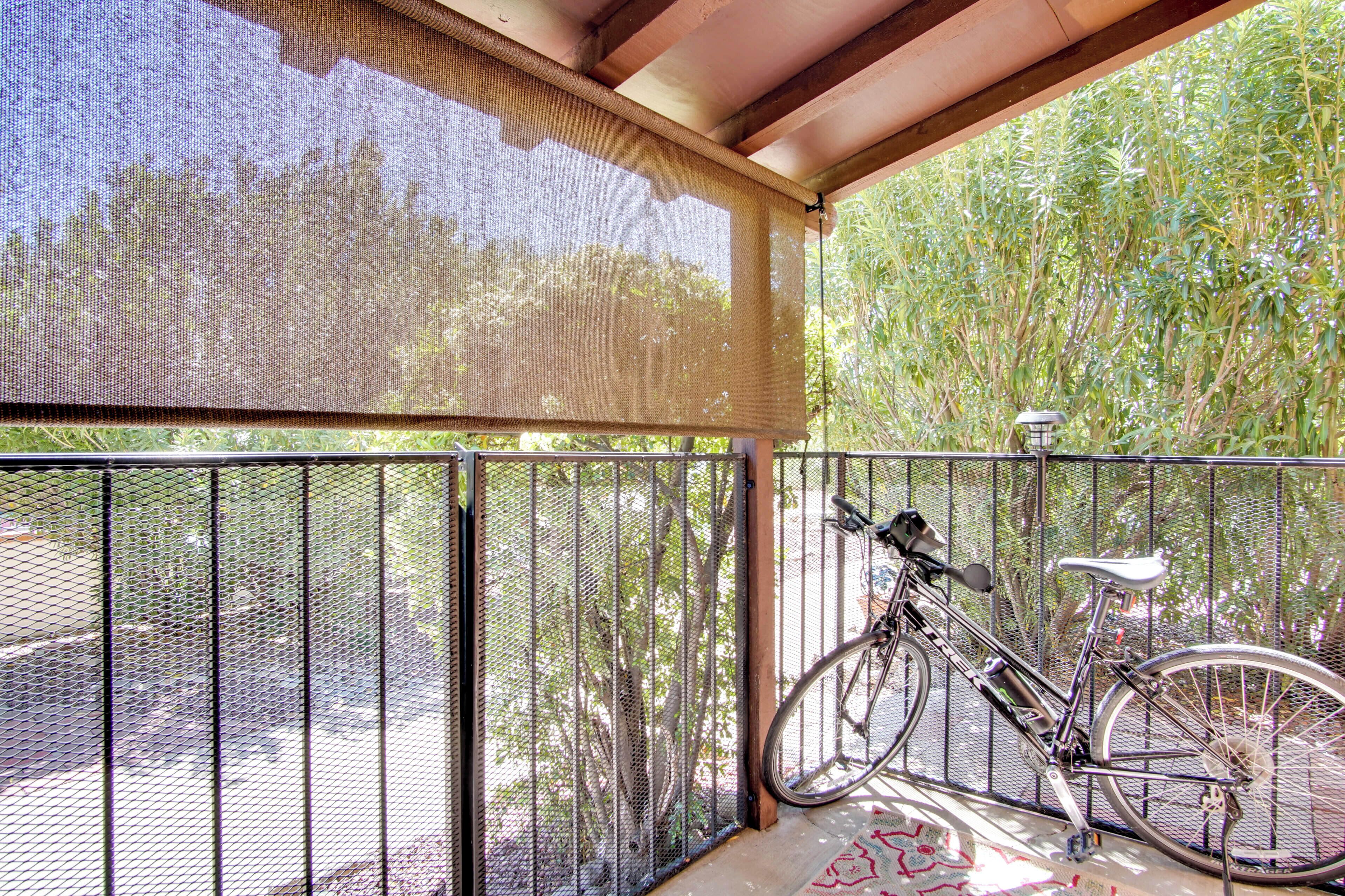 A covered balcony with a bicycle leaning against the railing, a mesh screen, and a view of greenery.