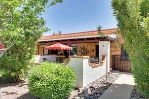 Un patio con una parrilla, mobiliario exterior y un paraguas rojo.