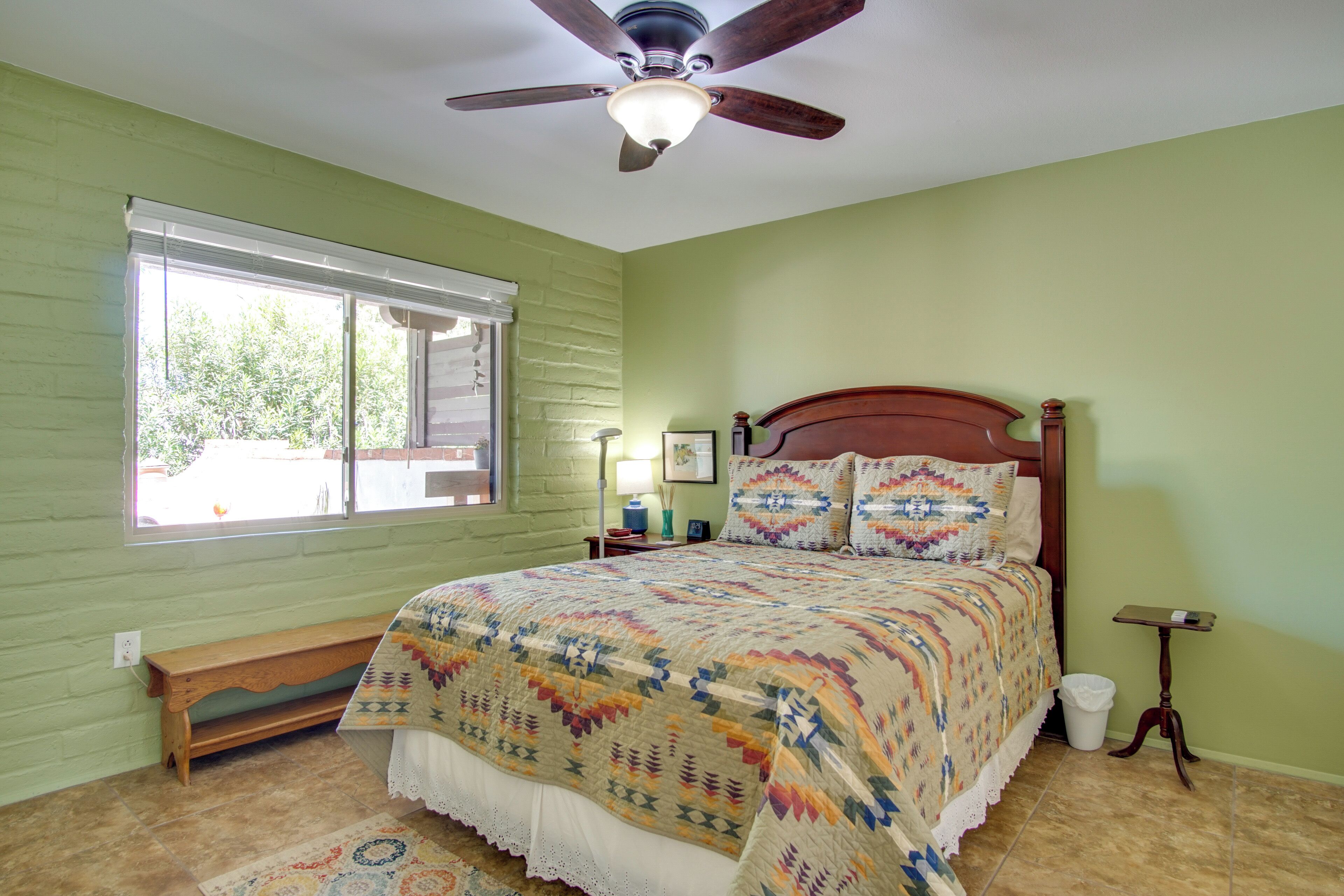 A bedroom with a wooden bed, a ceiling fan, a window with blinds, and a small bedside table.