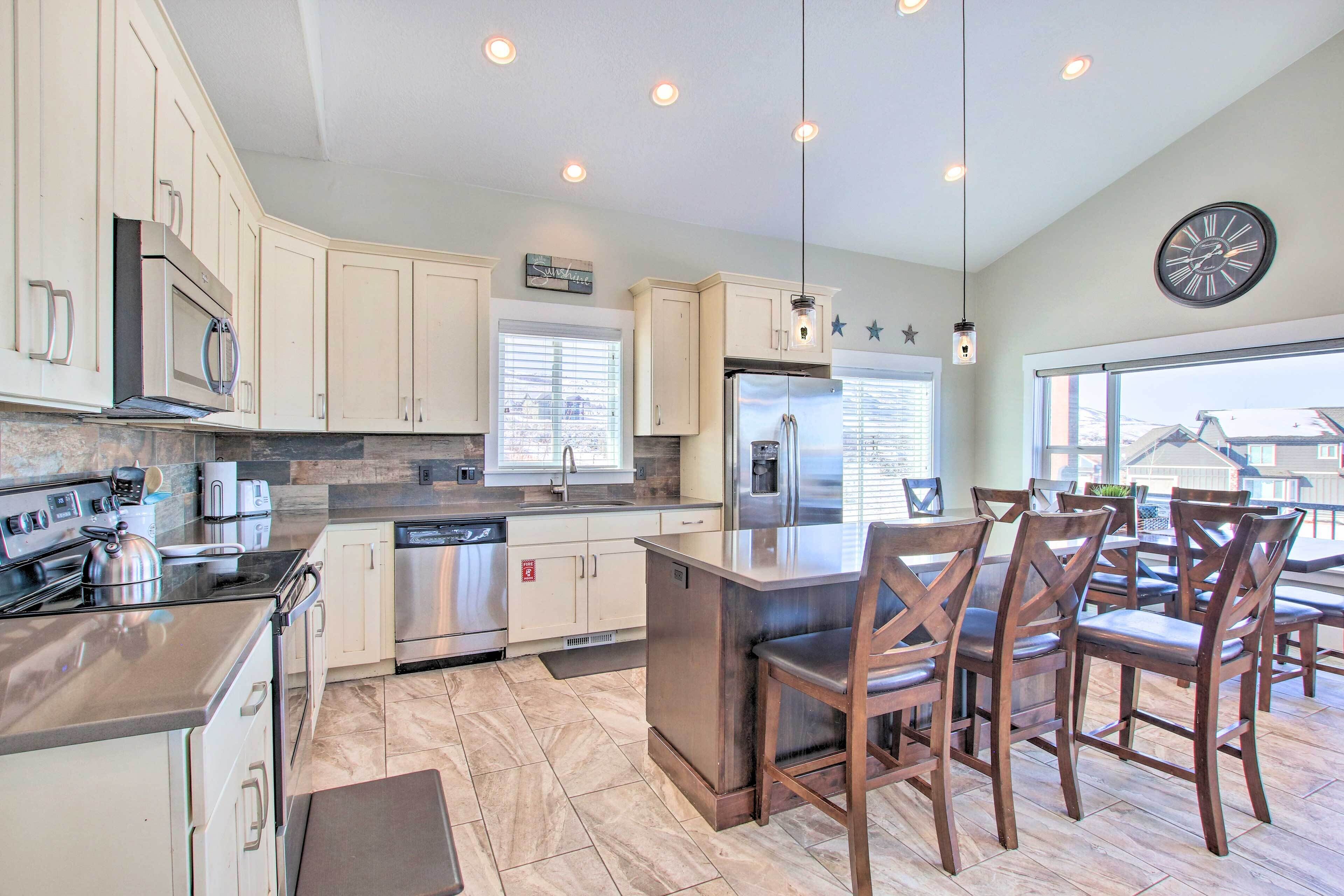 A modern kitchen with a central island, stainless steel appliances, and wooden chairs.