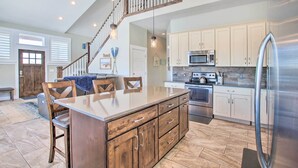 A kitchen with a central island, wooden cabinets, stainless steel appliances, and a staircase leading to an upper level. - Garden City Gem: Private Hot Tub & Game Room! (Garden City)