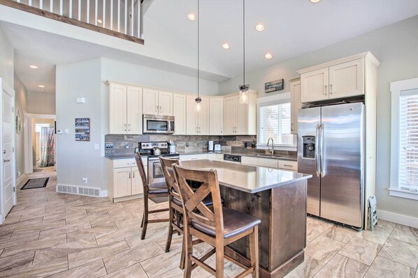 A spacious kitchen with a large island, stainless steel appliances, and wooden chairs.