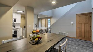 A modern kitchen with white cabinets, a microwave, and an oven. There is a dining table with a fruit bowl and a chair. - Luxurious Tacoma Retreat w/ Quartz Countertops! (Puyallup)