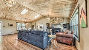 A spacious living room with a high ceiling, wooden flooring, a large sectional sofa, a smaller sofa, and a stone fireplace. - Ruidoso 'memories Mountain Retreat' w/ Hot Tub! (Ruidoso)