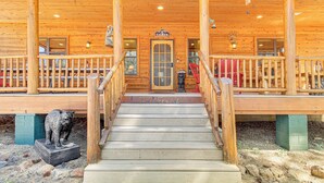 Une cabane en bois avec un porche, un escalier menant à l’entrée et une statue d’ours sur la gauche.